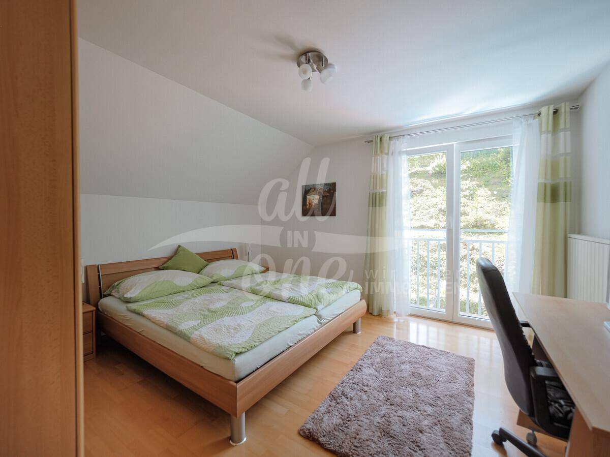 Schlafzimmer mit Holzboden, Zugang zum französischen Balkon und Schreibtisch.