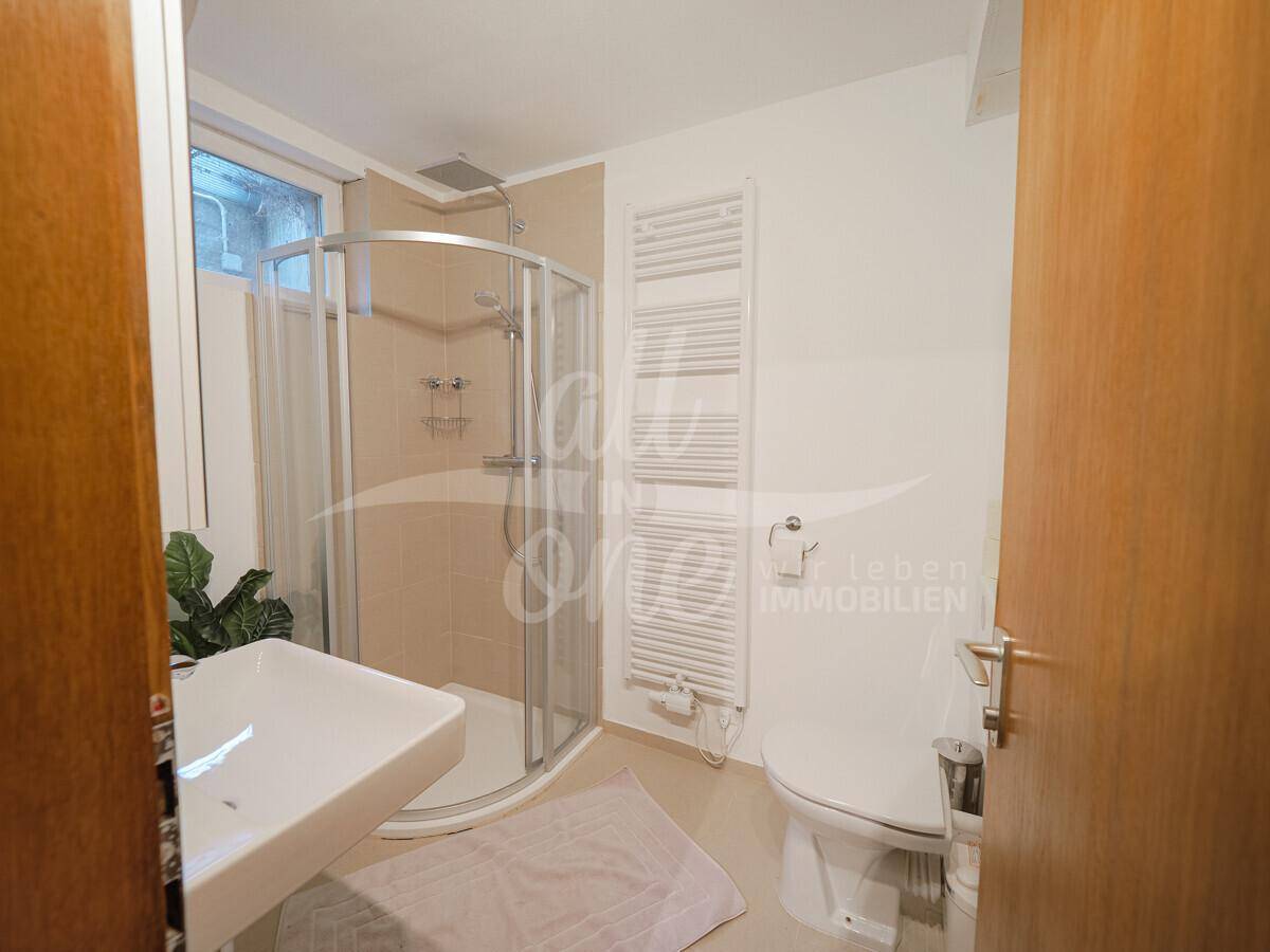 Modernes Badezimmer mit Duschkabine, Waschbecken und beheiztem Handtuchhalter.