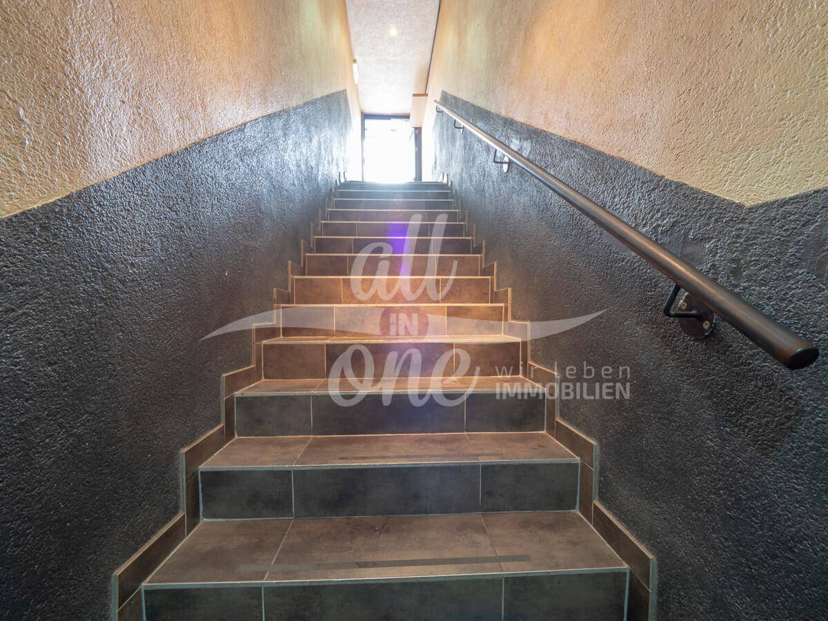 Geflieste Treppe mit Handlauf, die zu einem oberen Bereich führt, beleuchtet durch natürliches Licht.