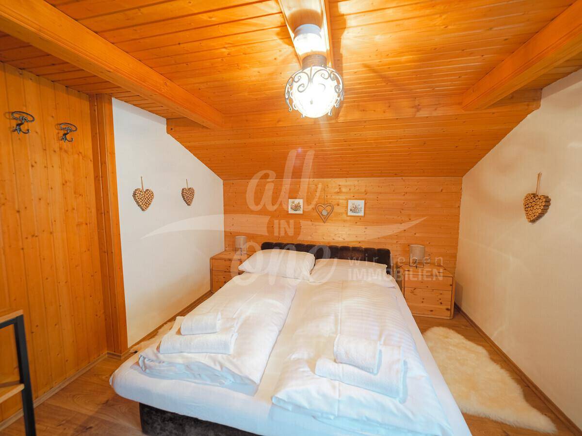 Gemütliches Schlafzimmer im Dachgeschoss mit Holzverkleidung und Doppelbett.
