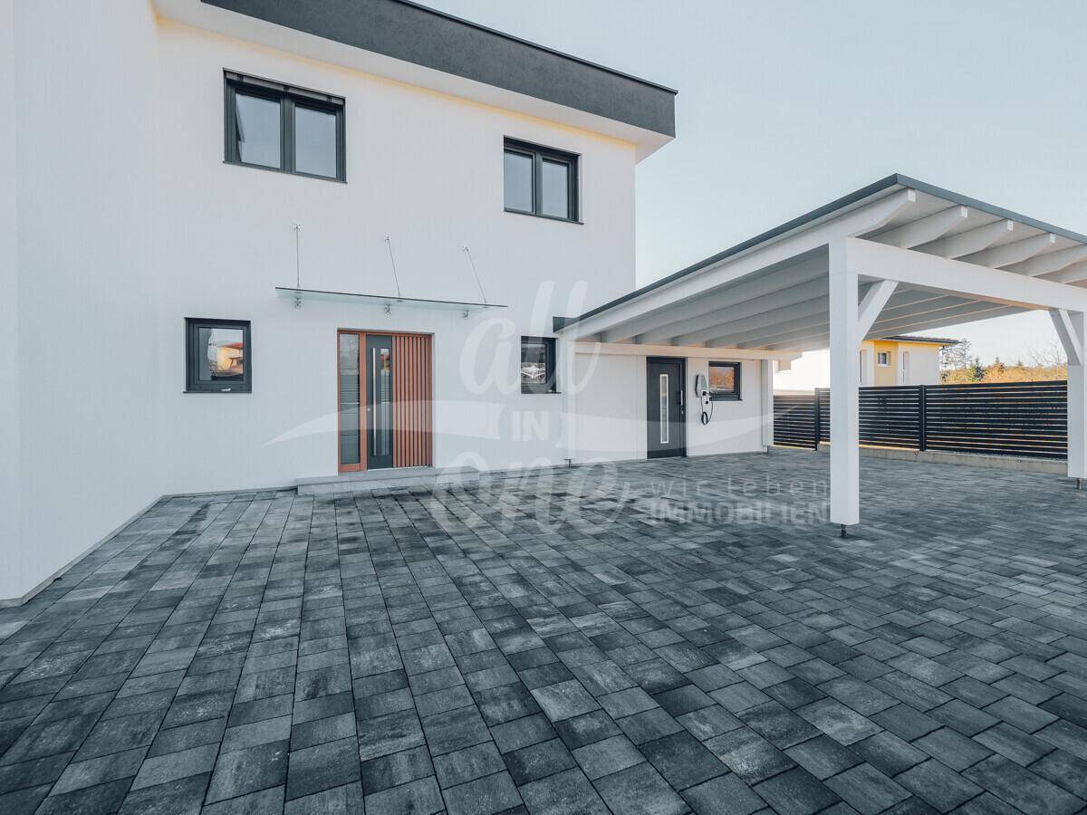 Moderne Hausfront mit gepflasterter Einfahrt und einem überdachten Carport.