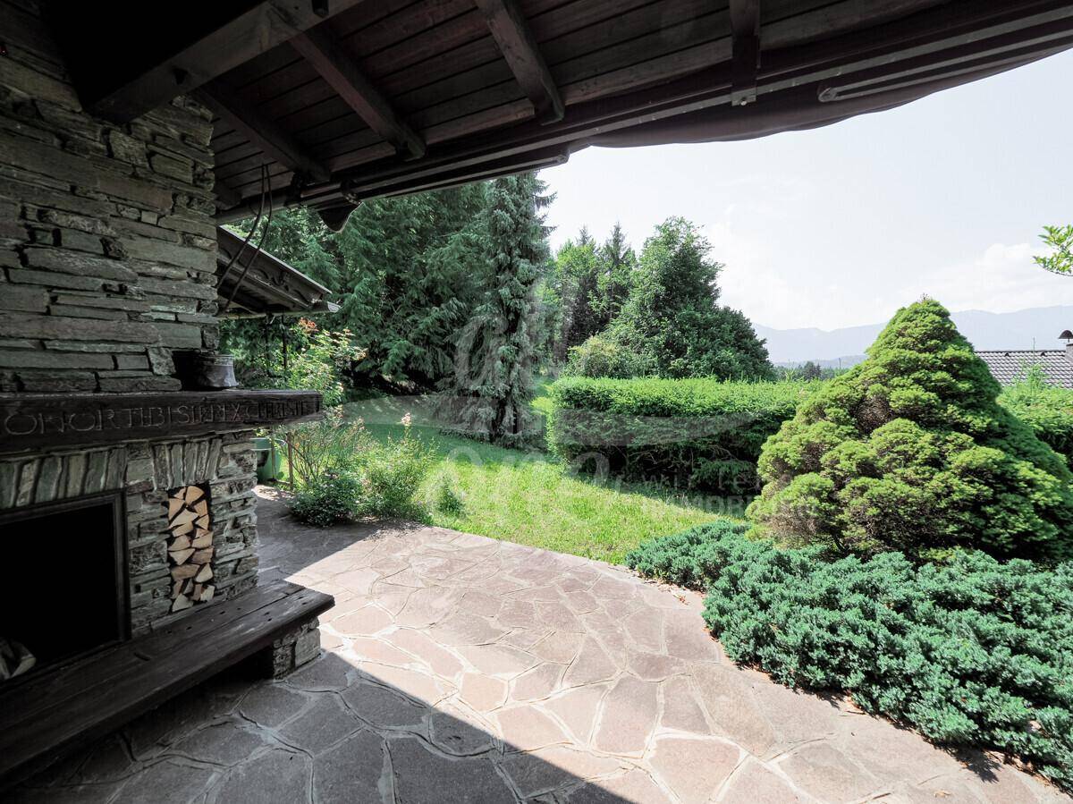 Überdachte Terrasse mit rustikalem Steinkamin und Blick auf den gepflegten Gartenbereich.