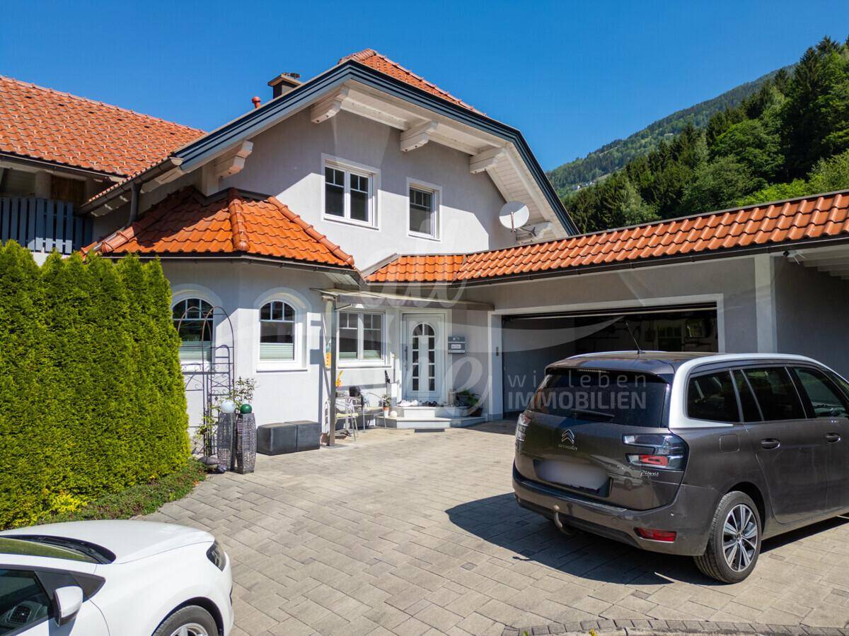 Gepflegtes Einfamilienhaus mit Garage, gepflasterter Auffahrt und herrlichem Bergblick unter blauem Himmel.