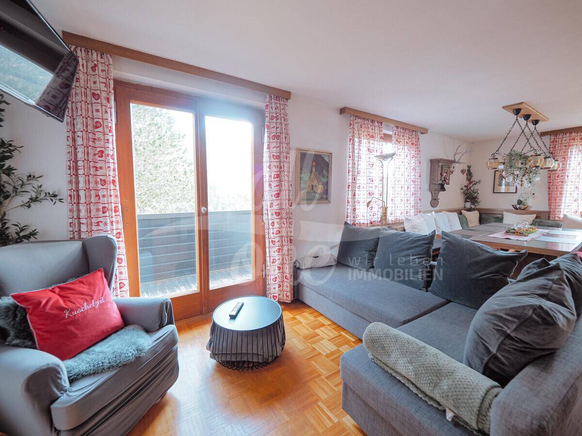 Heller Wohnbereich mit bequemer Couch, Parkettboden und Zugang zum Balkon.