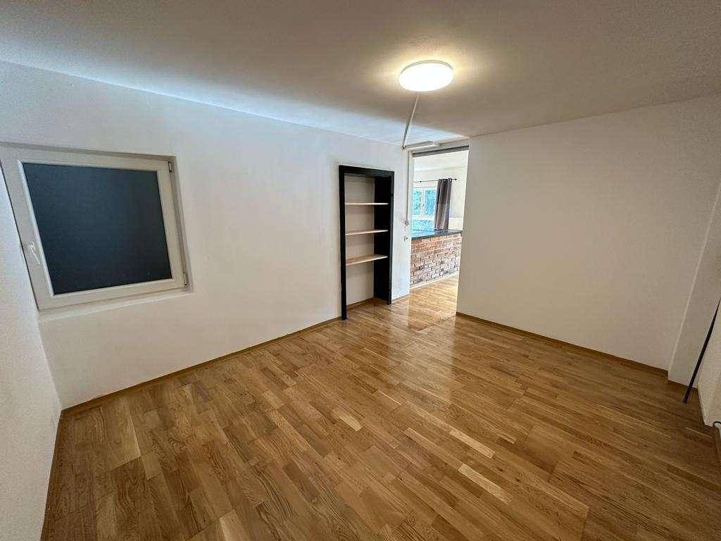 Heller Raum mit Holzboden und Regal, offen zu einem weiteren Bereich.