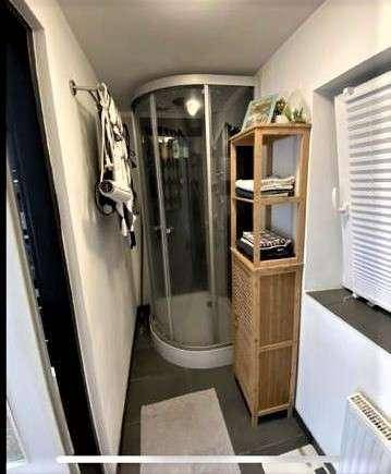Kleines Badezimmer mit runder Duschkabine, Regal und Fenster für Tageslicht.