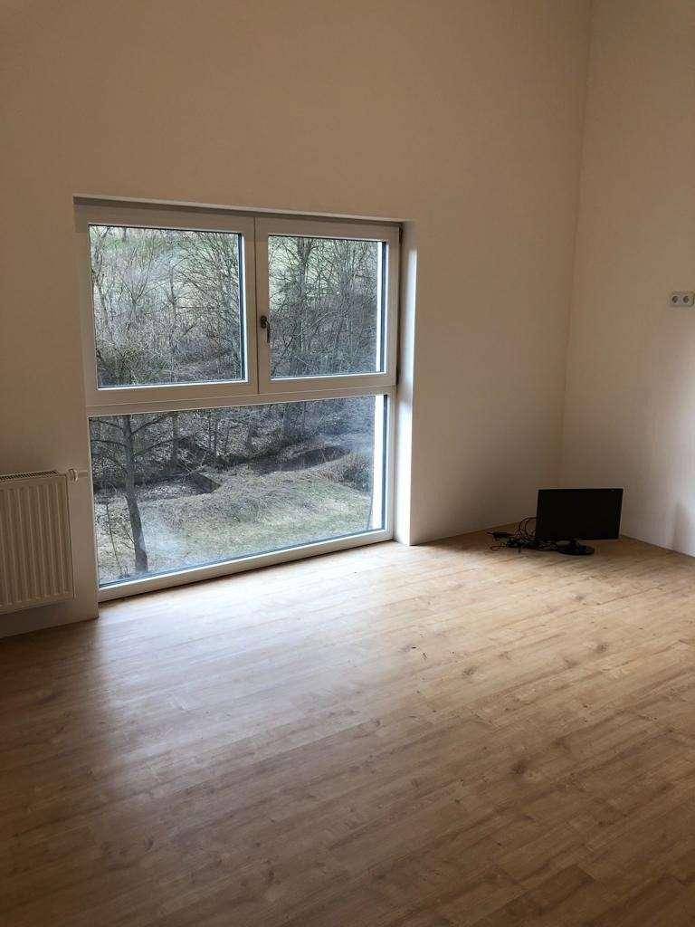 Heller, unmöblierter Raum mit großem Fenster und Blick auf grüne Bäume.