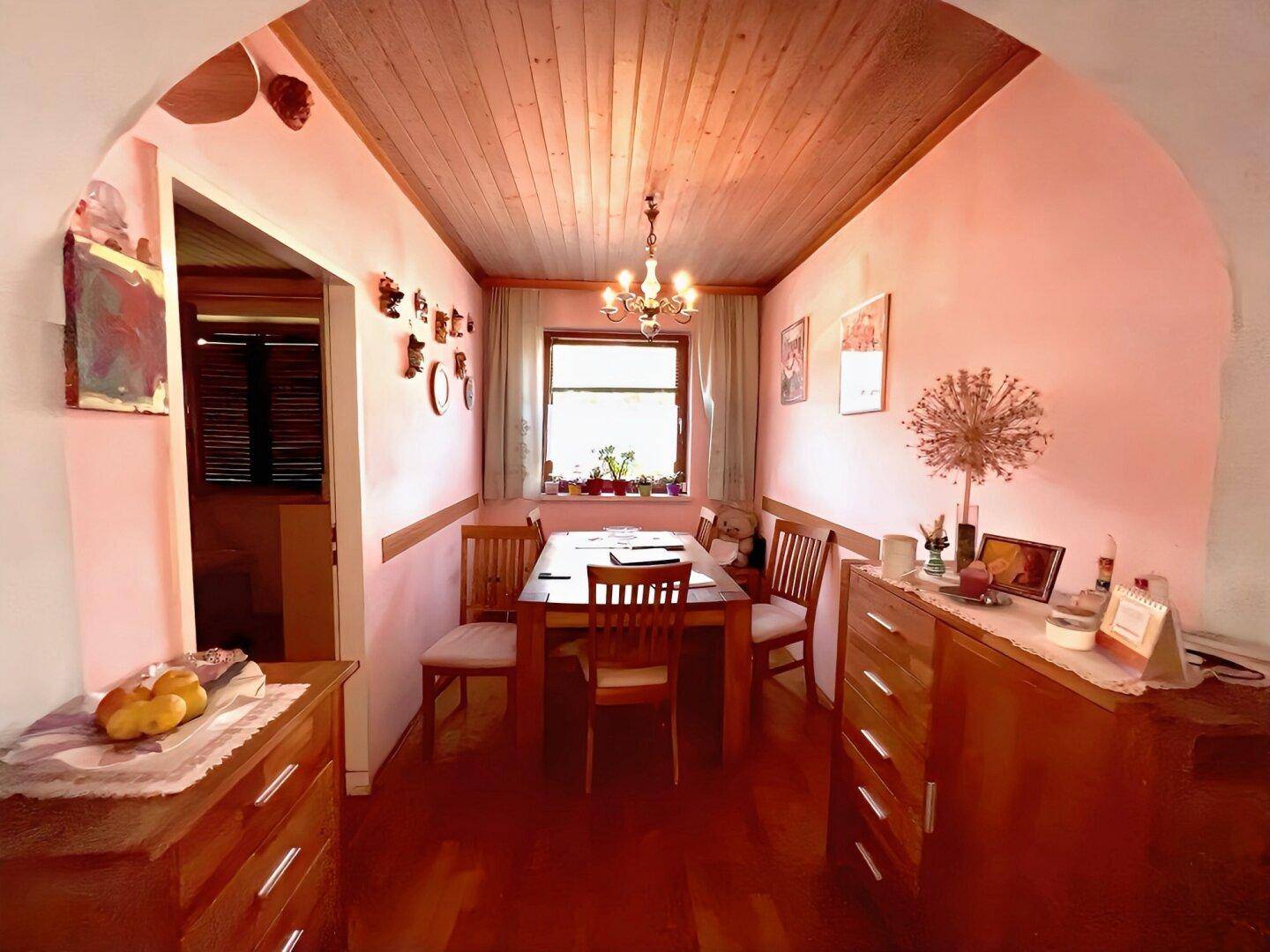 Esszimmer mit rosafarbenen Wänden, Holzbalkendecke und Esstisch am Fenster.