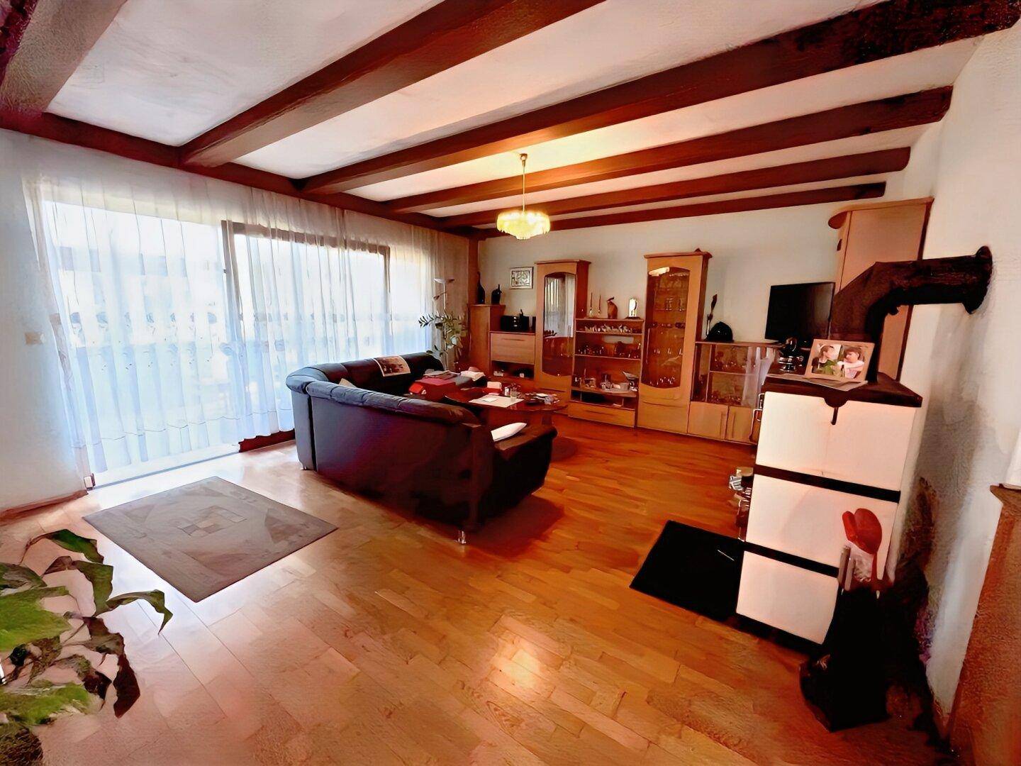 Geräumiges Wohnzimmer mit Holzbalkendecke, Parkettboden und Zugang zur Terrasse.