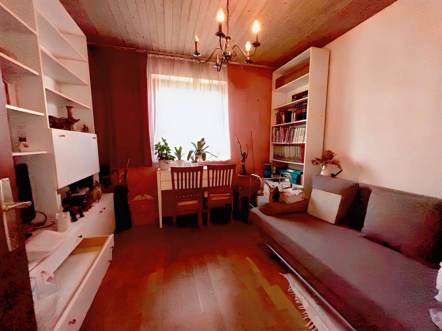 Arbeitszimmer mit Bücherregalen, Sofa und Schreibtisch am Fenster.