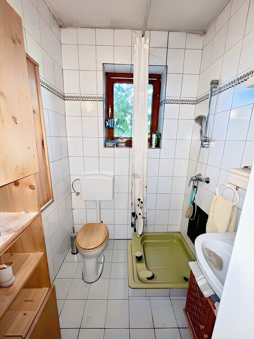 Badezimmer mit weißen Fliesen, Dusche und Fenster für natürliche Belüftung.