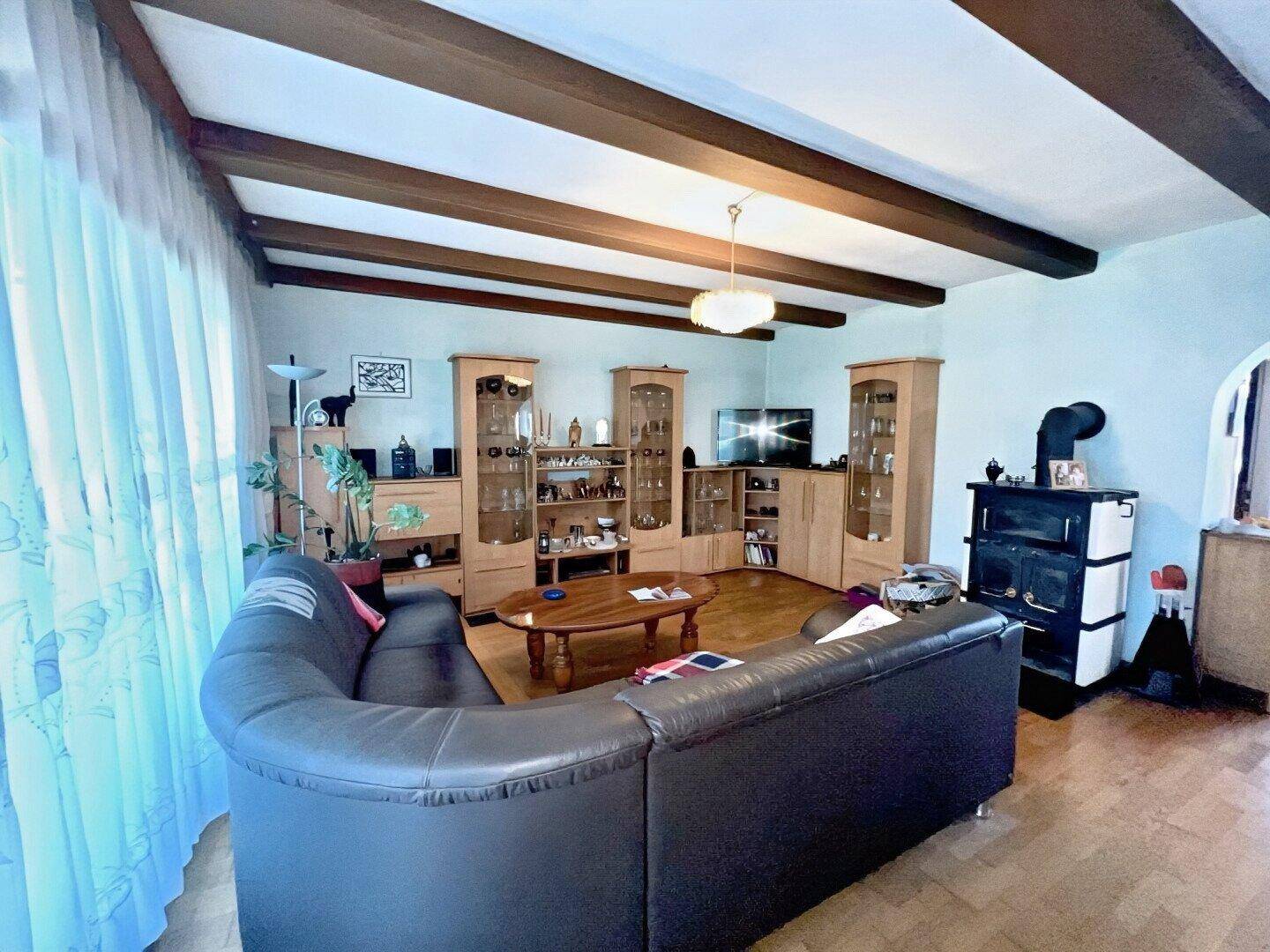 Gemütliches Wohnzimmer mit Holzbalkendecke, Parkettboden und Kaminofen.