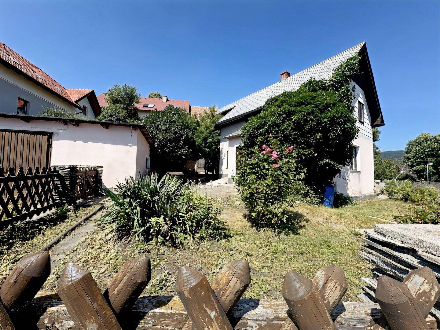 Gartenbereich hinter dem Haus mit verschiedenen Pflanzen, einem Weg und rustikalem Holzzaun.