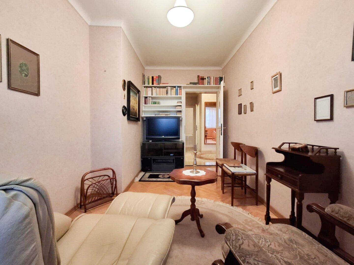 Wohnzimmer mit Fernseher, Bücherregal und bequemen Sitzgelegenheiten.