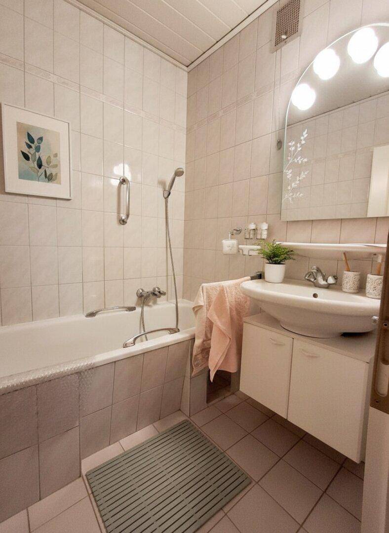Badezimmer mit Badewanne, Waschbecken und hellen Fliesen.