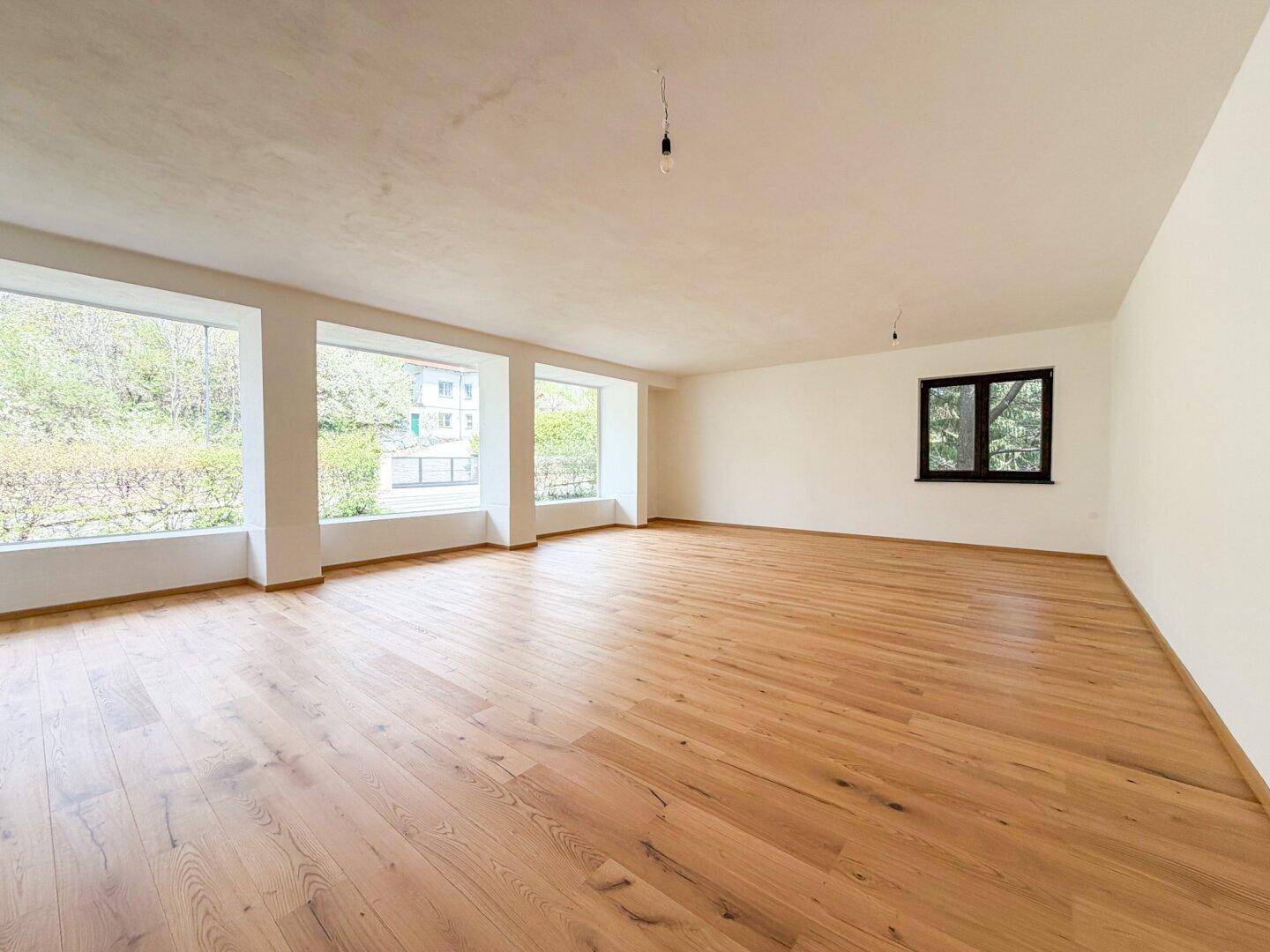 Geräumiger, heller Raum mit Holzboden und großen Fenstern, die einen weiten Blick ins Grüne bieten.