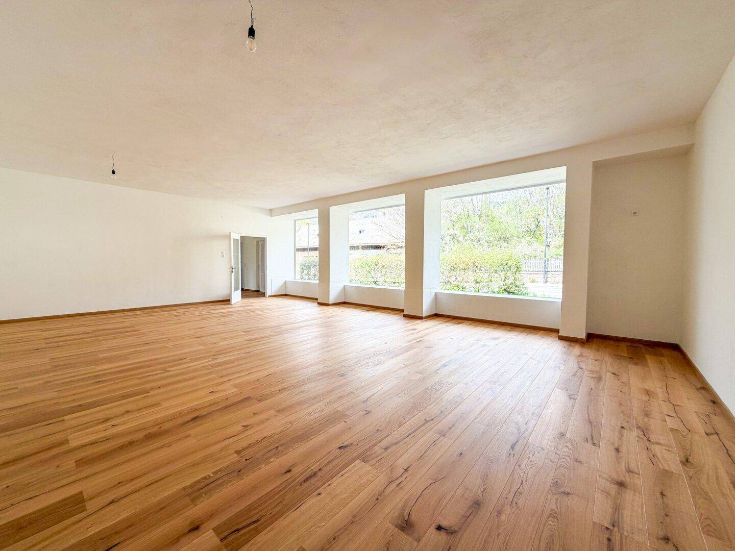 Weitläufiger, heller Raum mit Holzboden und großen Fenstern, der vielfältige Nutzungsmöglichkeiten bietet.