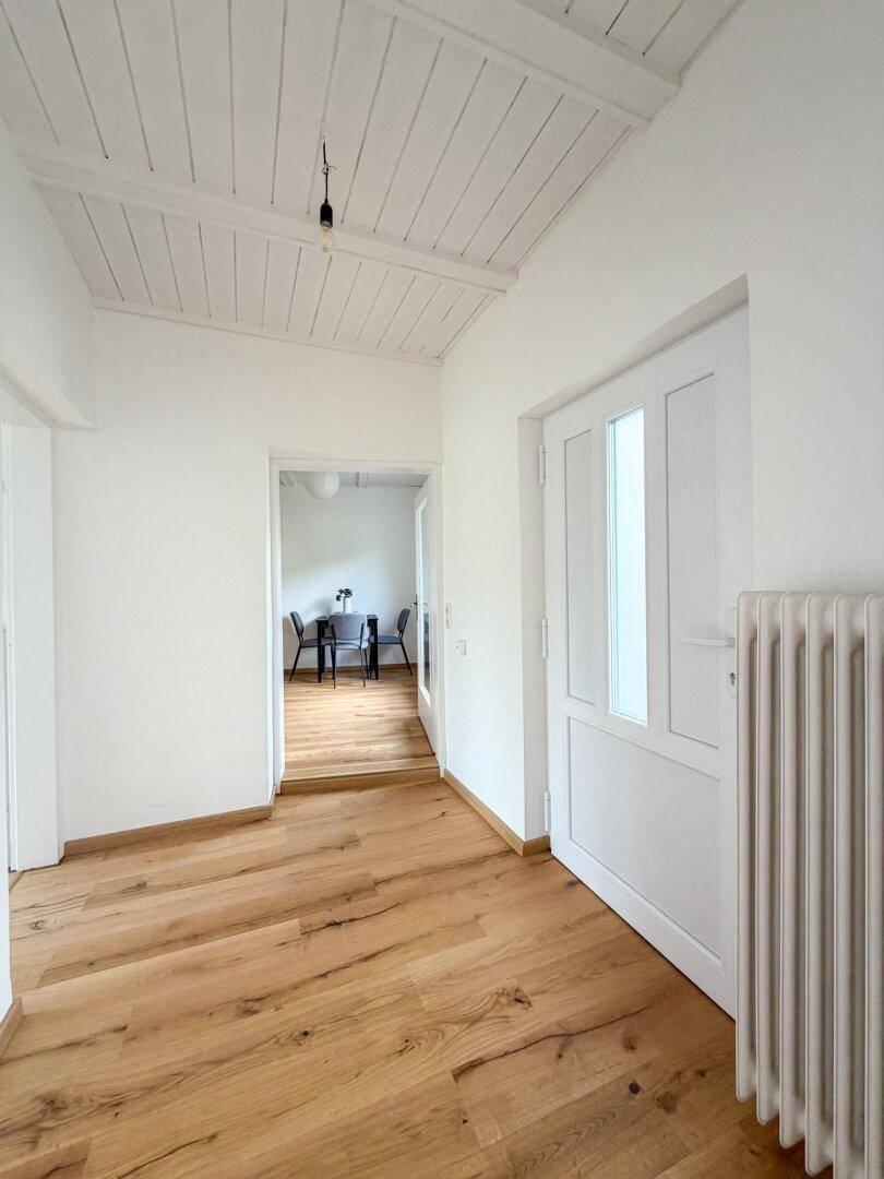 Geräumiger Flur mit Holzboden und weißer Decke, der den Blick in einen angrenzenden Essbereich freigibt.