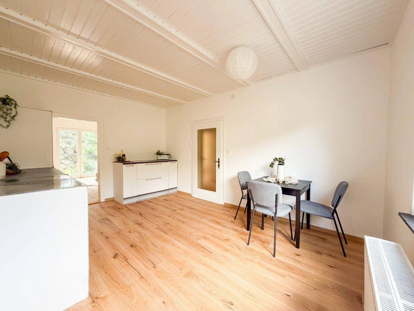 Helle Küche mit Essbereich, Holzboden und weißen Schränken unter einer Holzdeckenverkleidung.