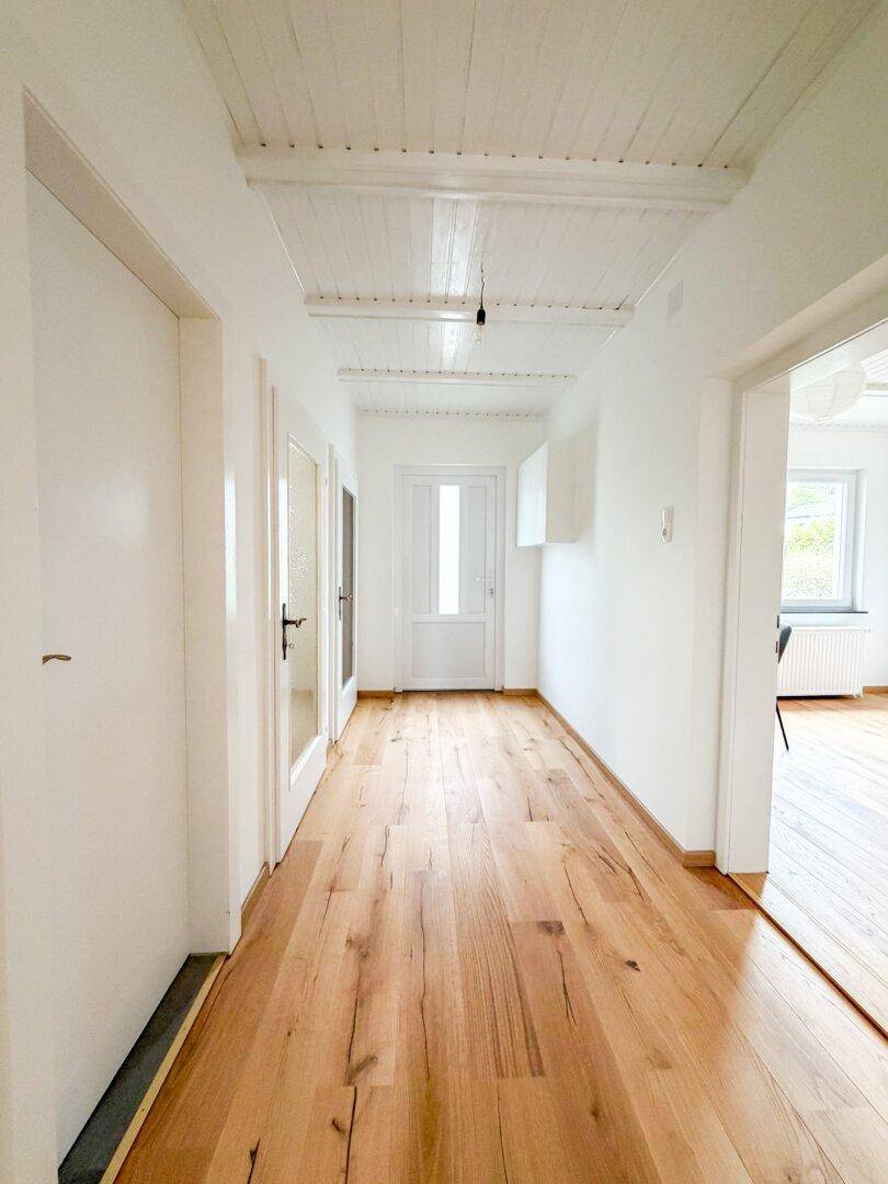 Langer, heller Flur mit Holzboden und weißer Deckenverkleidung, der verschiedene Räume verbindet.