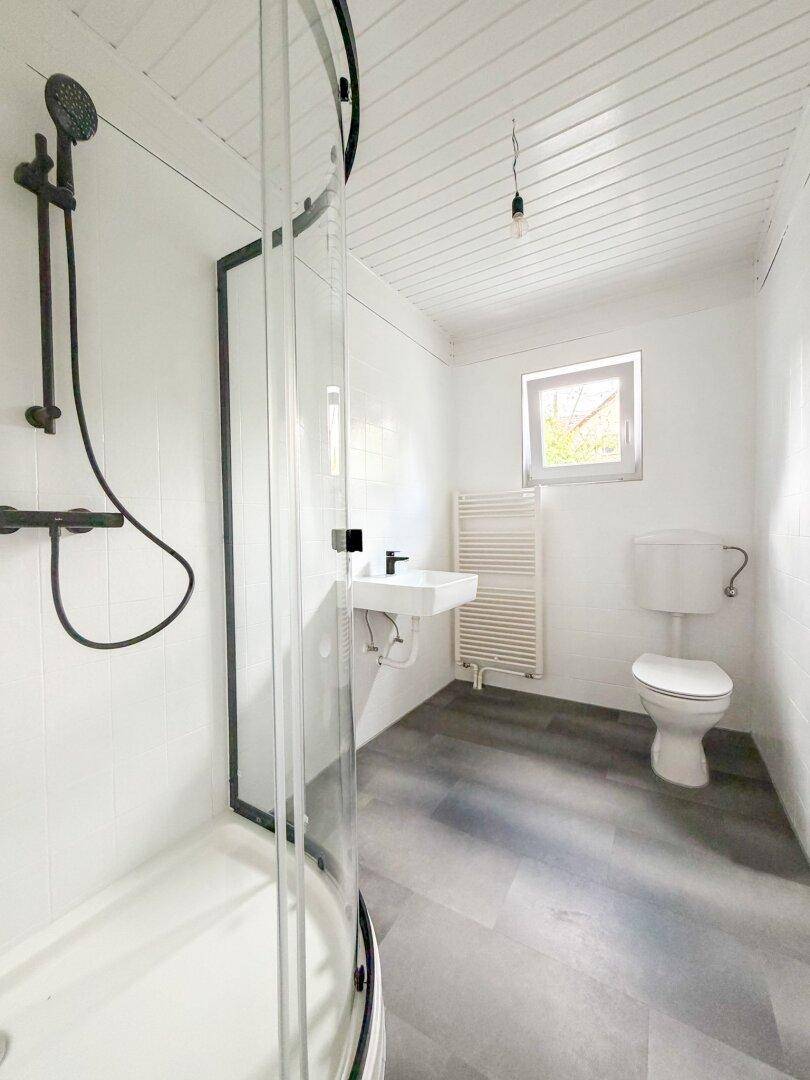 Modernes Badezimmer mit Dusche, Waschbecken und WC, ausgestattet mit weißen Fliesen und dunklem Boden.