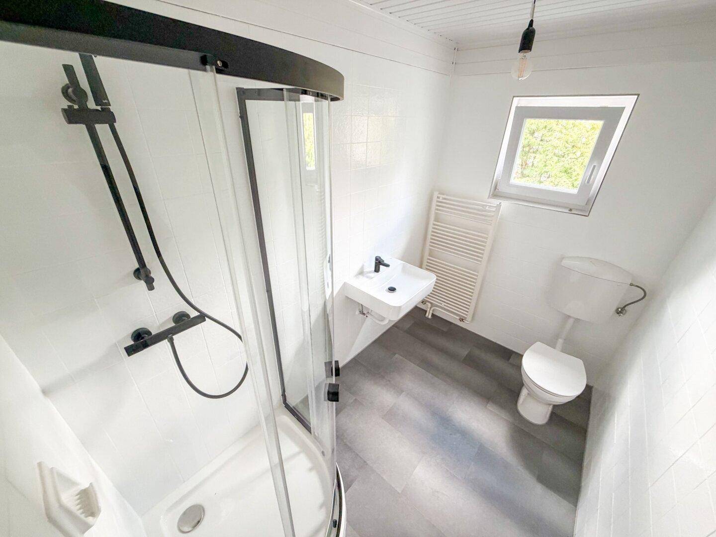 Helles Badezimmer mit Duschkabine, modernem Waschbecken und Fenster für natürliche Belüftung.