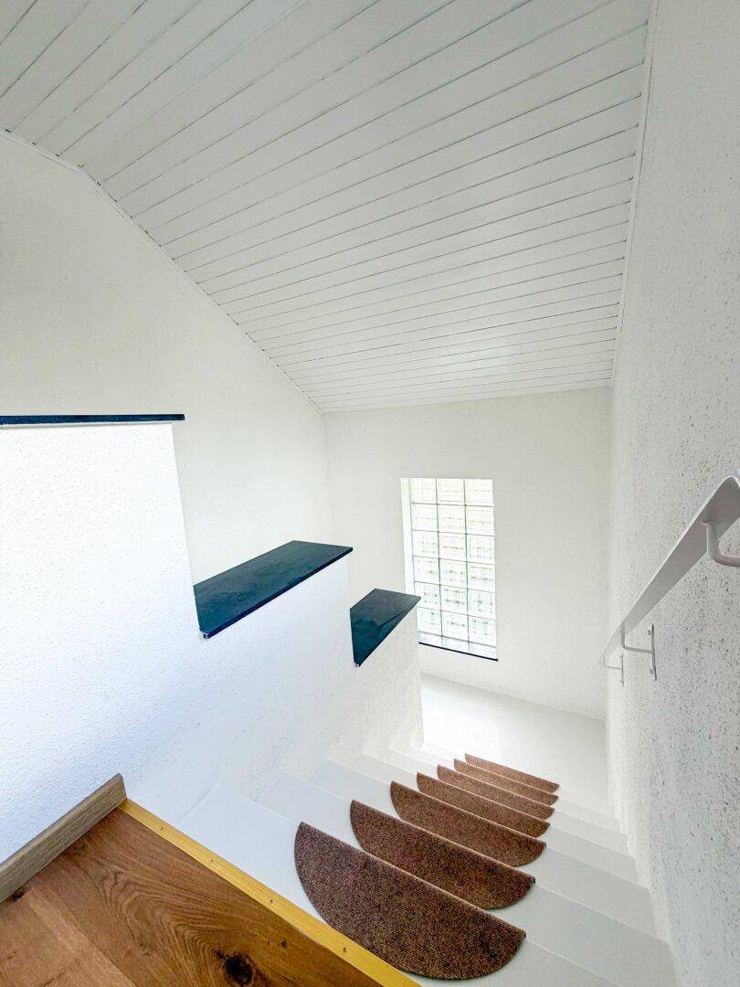Treppenhaus mit weißer Struktur und einem Fenster, das den Bereich mit natürlichem Licht erhellt.