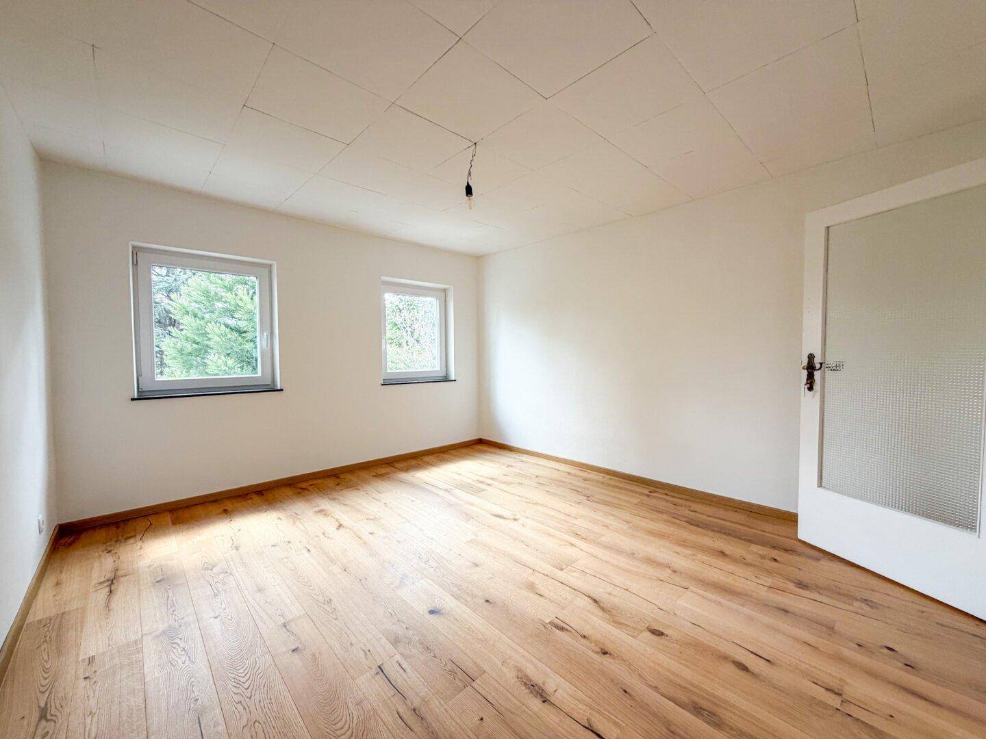 Helles Schlafzimmer mit Holzboden und weiß gestrichenen Wänden, bereit zur individuellen Gestaltung.