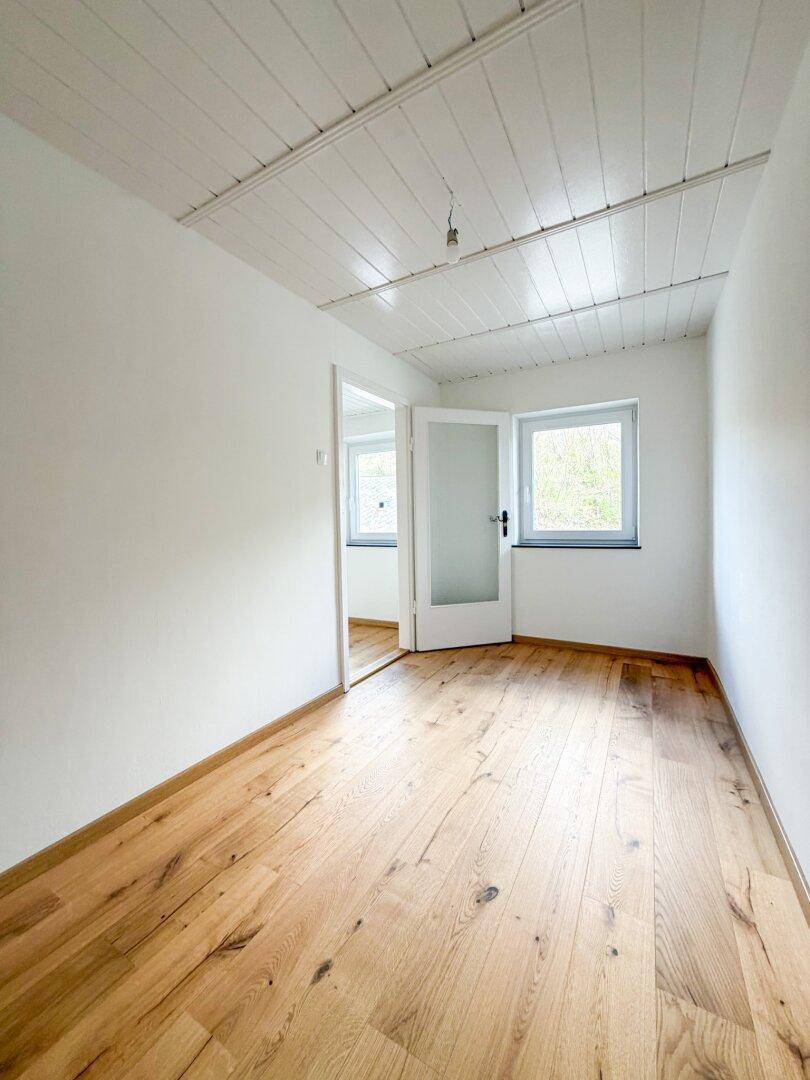 Kleineres Schlafzimmer mit Holzboden und Fenster, das viel Tageslicht in den Raum lässt.
