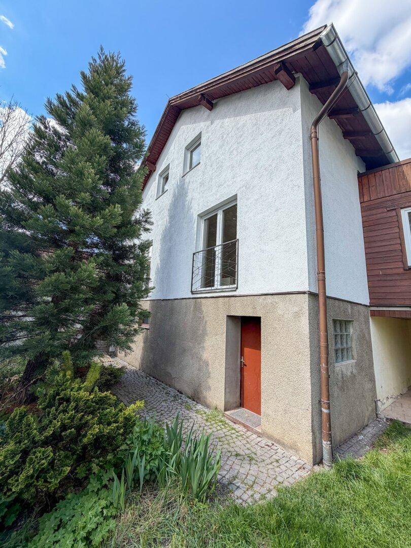 Seitenansicht des Hauses mit weißer Fassade, kleinem französischen Balkon und Zugang zum Gartenbereich.