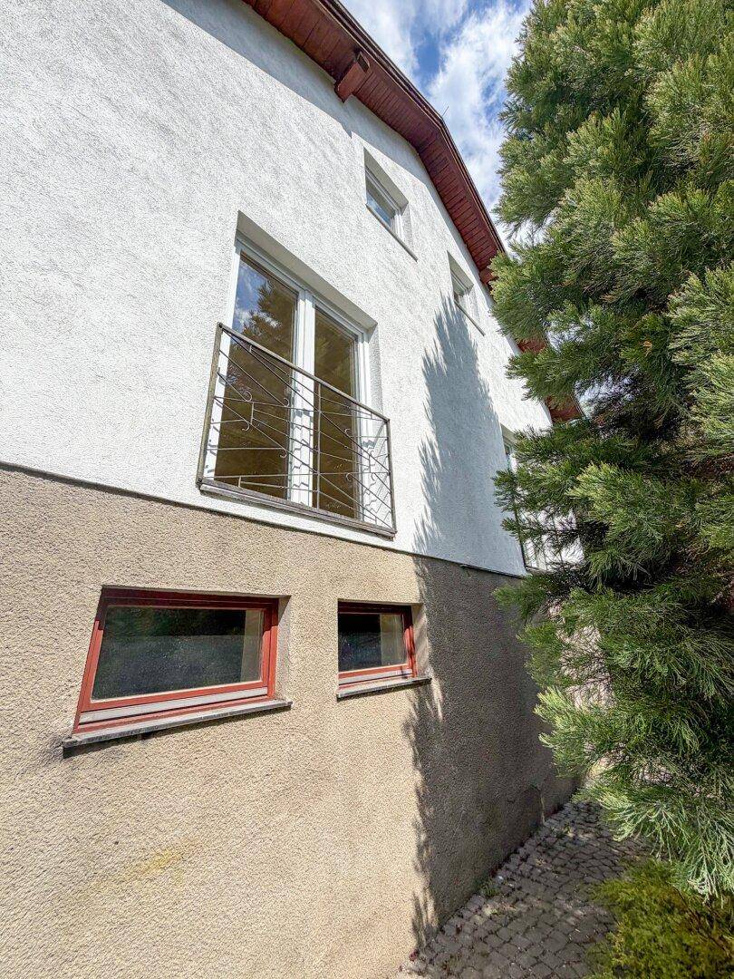 Seitenansicht des Hauses mit weißer Fassade, französischem Balkon und Fenstern im Untergeschoss.