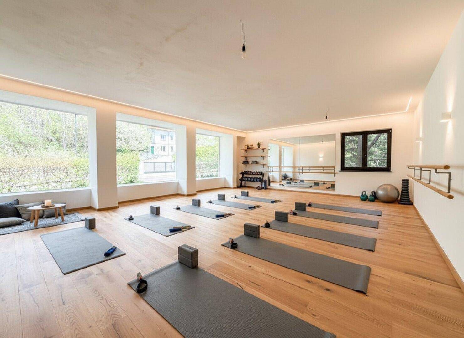 Moderner Fitnessraum mit Holzboden, großen Fenstern und Ausstattung für Sport und Wellness.
