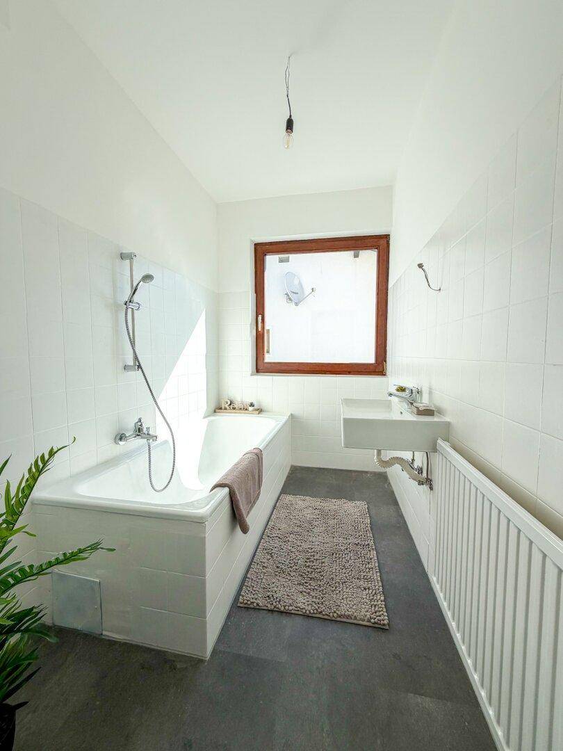 Helles Badezimmer mit Badewanne, Waschbecken, weißen Fliesen und Fenster.