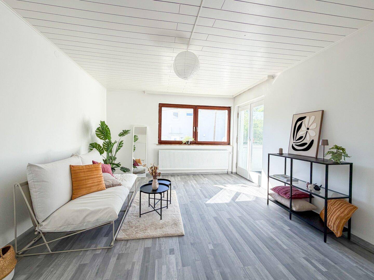 Freundliches Wohnzimmer mit hellem Laminatboden, moderner Dekoration und Balkonzugang.
