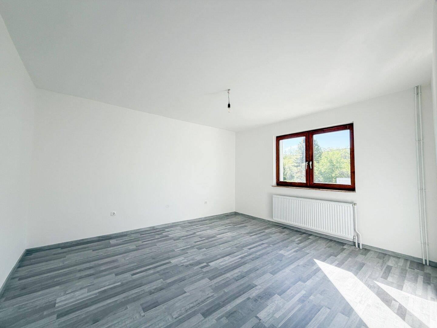 Geräumiges Schlafzimmer mit Laminatboden, weiß gestrichenen Wänden und großem Fenster.
