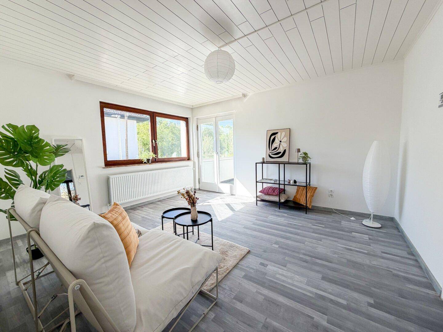 Geräumiges Wohnzimmer mit viel Tageslicht, modernem Interieur und Zugang zum Balkon.