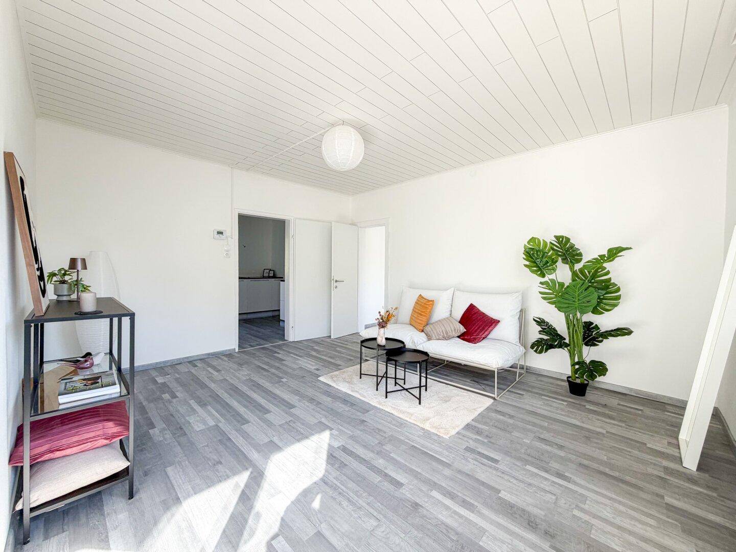 Modern eingerichtetes Wohnzimmer mit viel Tageslicht und schlichtem Design.