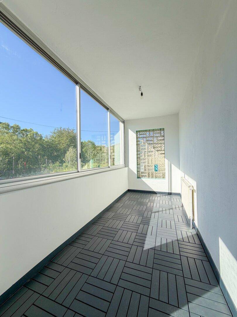 Helle Loggia mit großen Fenstern, dunklem Fliesenboden und Blick ins Grüne.