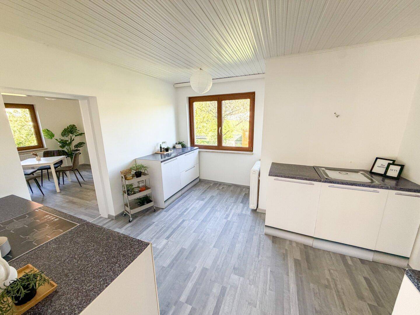 Funktionale Küche mit weißen Unterschränken, Laminatboden und Blick in den Essbereich.