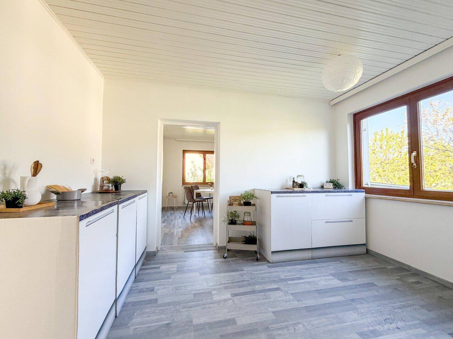 Helle Küche mit schlichten weißen Schränken, Laminatboden und Fenster mit Ausblick.