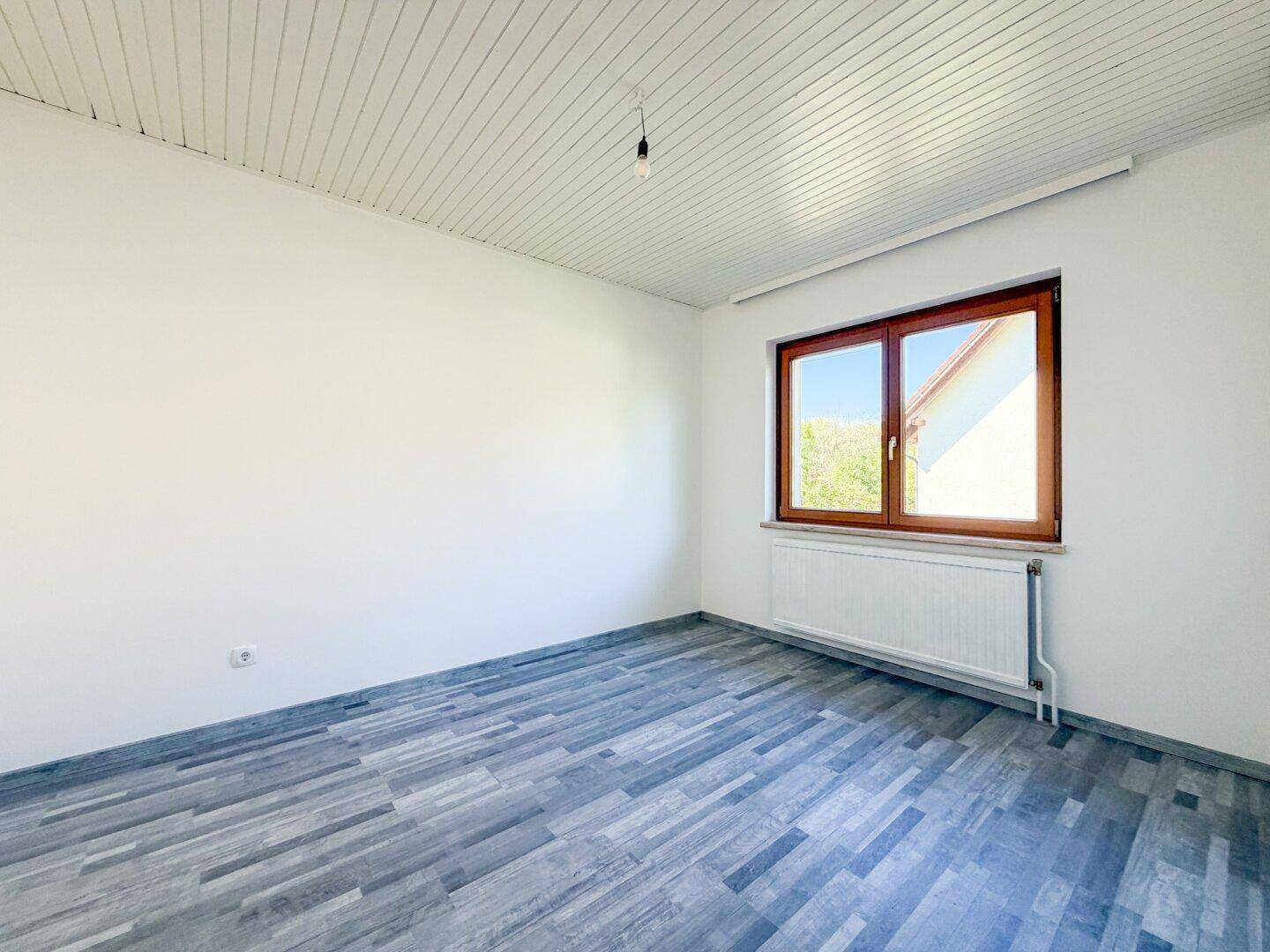 Geräumiges Schlafzimmer mit Laminatboden, weißen Wänden und großem Fenster.