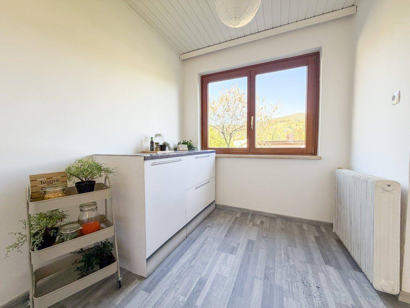 Kleine, helle Küche mit Fenster, Laminatboden und ausreichend Arbeitsfläche.