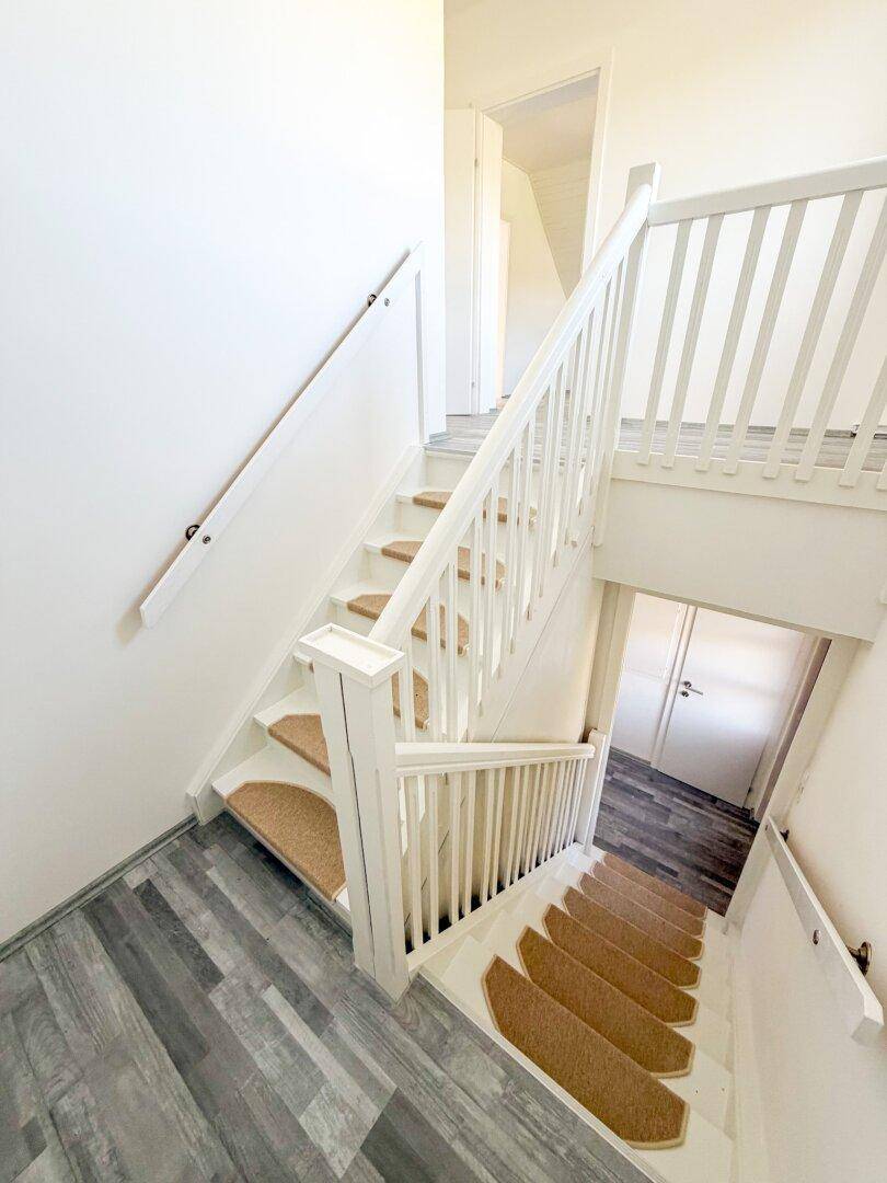 Treppenhaus mit hellem Laminatboden, weißem Geländer und Teppichstufen.