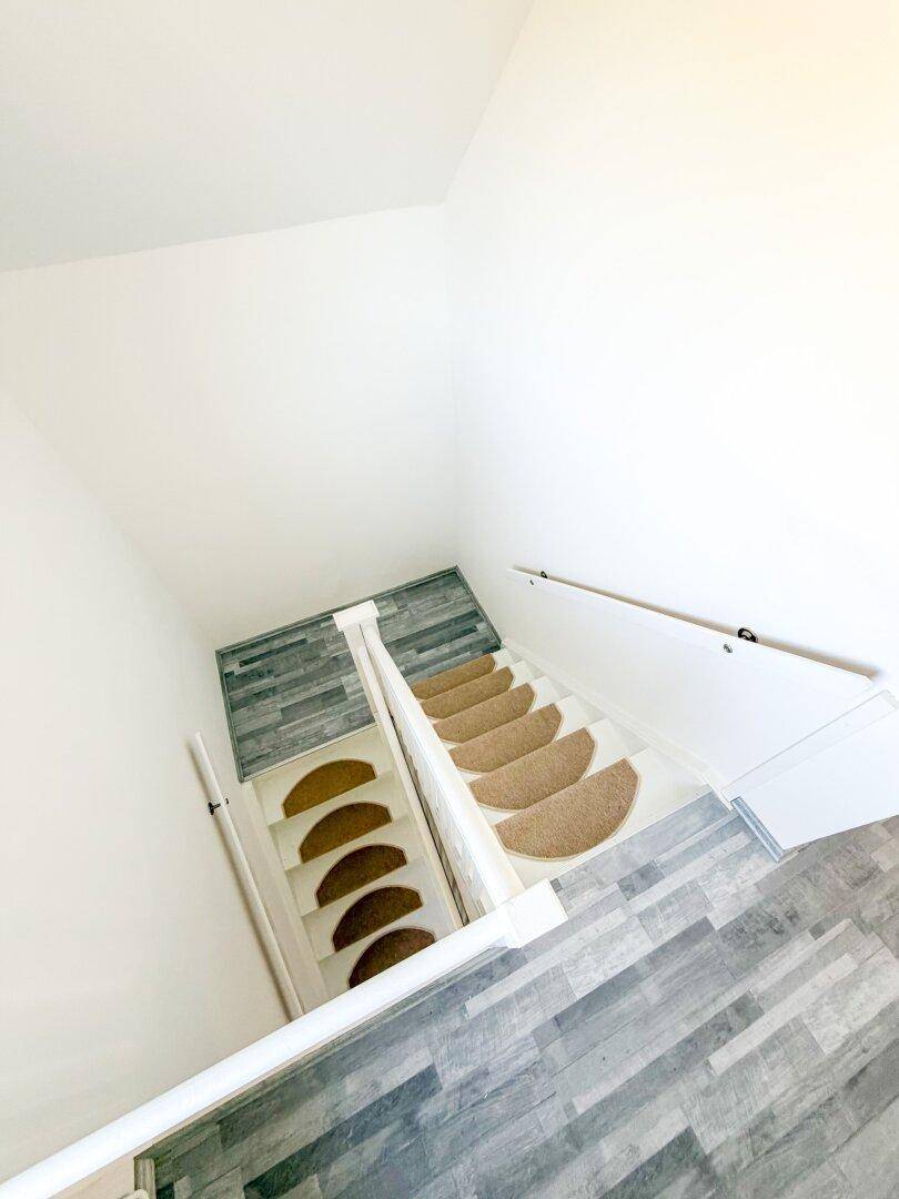Treppenaufgang mit Teppichstufen, hellem Laminatboden und weißem Geländer.