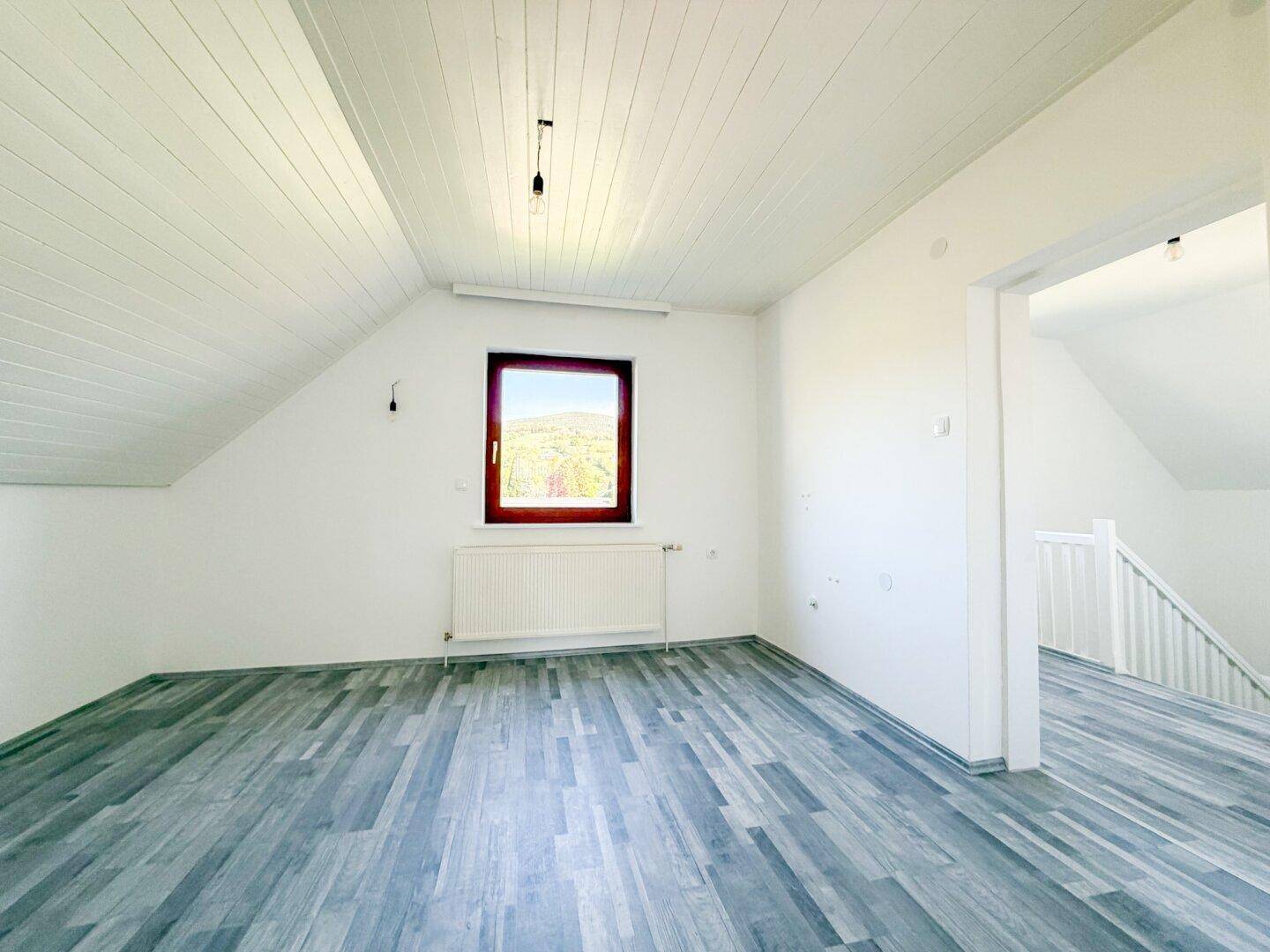 Geräumiges Schlafzimmer im Dachgeschoss mit Laminatboden und Fenster.