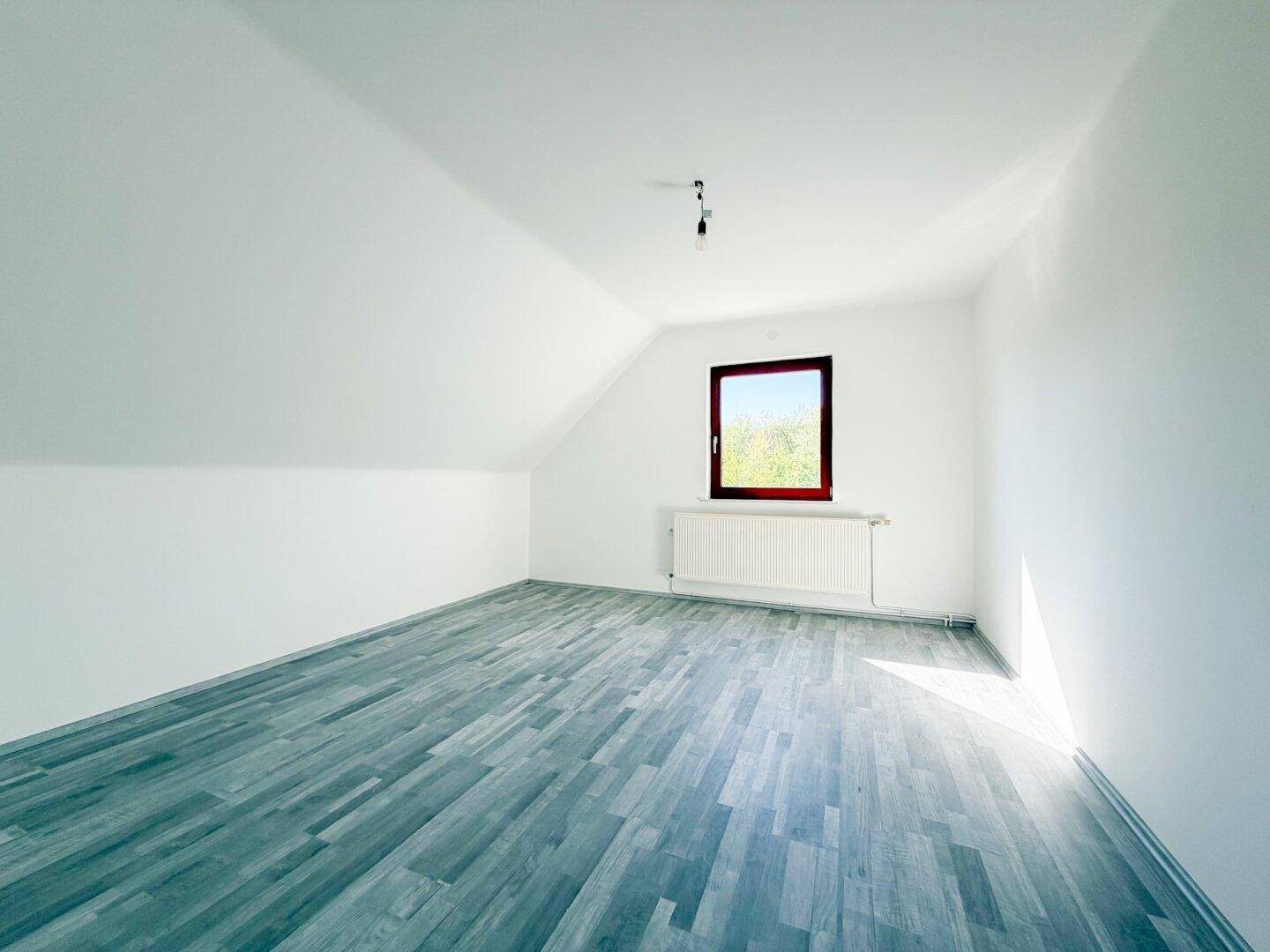 Helles Schlafzimmer im Dachgeschoss mit Laminatboden und Fenster.