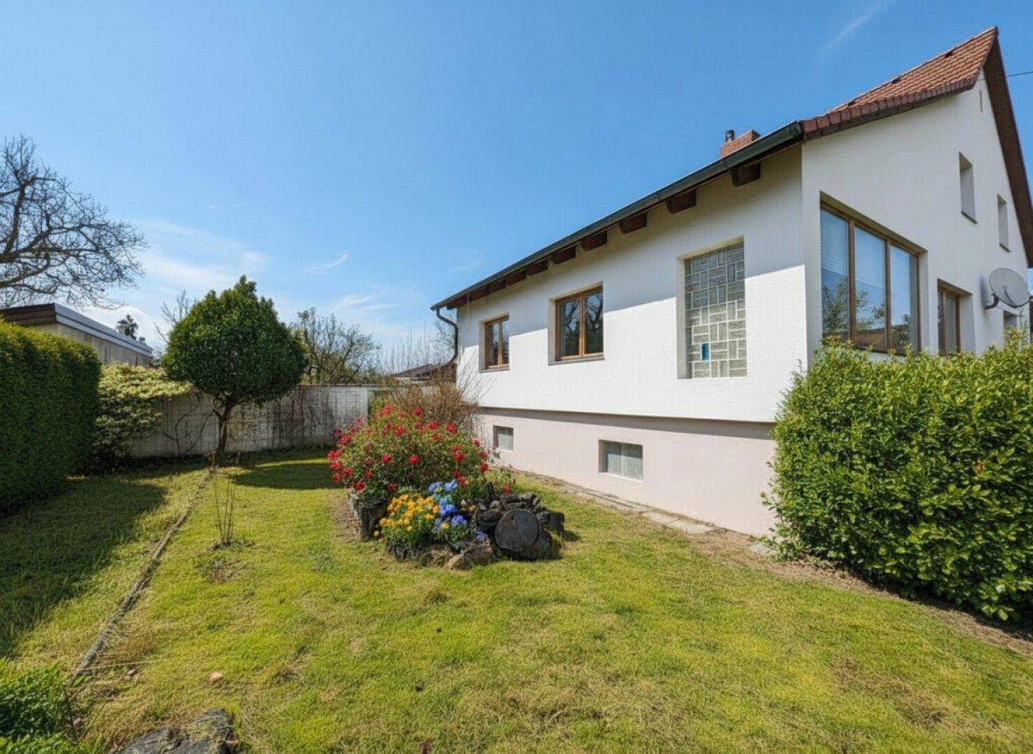 Gepflegter Gartenbereich neben dem Haus mit Rasenfläche und bunten Blumenbeeten.