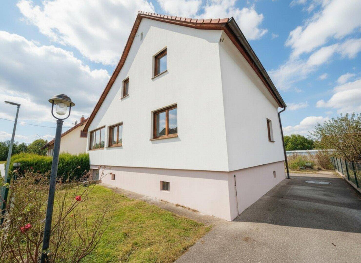 Rückansicht des Hauses mit Zufahrt und kleinem Gartenbereich unter bewölktem Himmel.