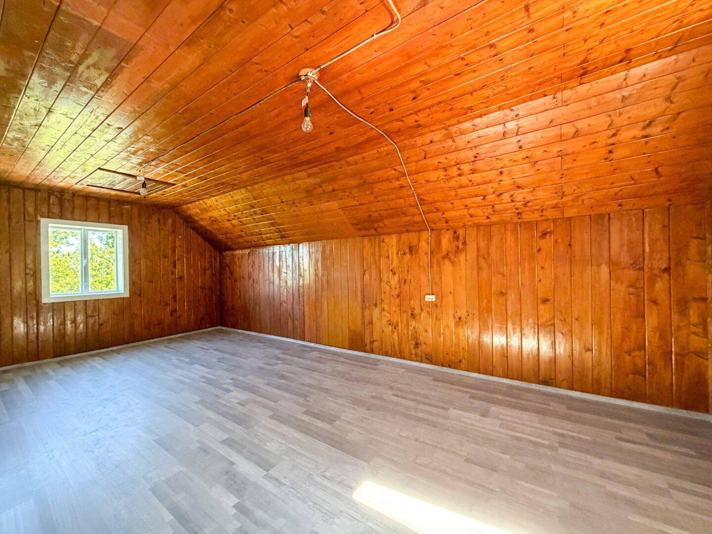 Geräumiges Dachzimmer mit Holzverkleidung an Wänden und Decke sowie hellem Laminatboden.