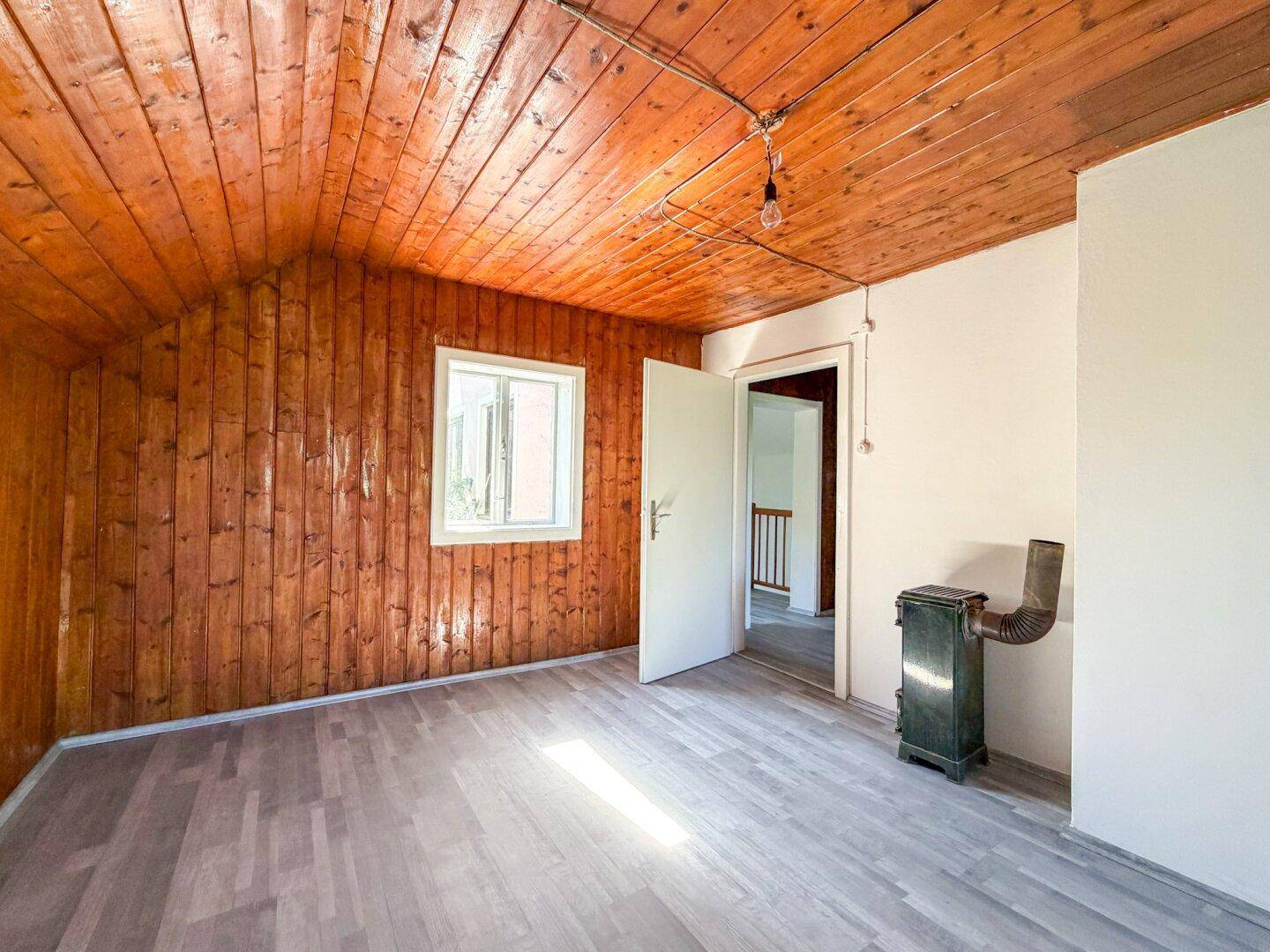 Gemütliches Dachzimmer mit Holzverkleidung an Wänden und Decke sowie einem Ofen.